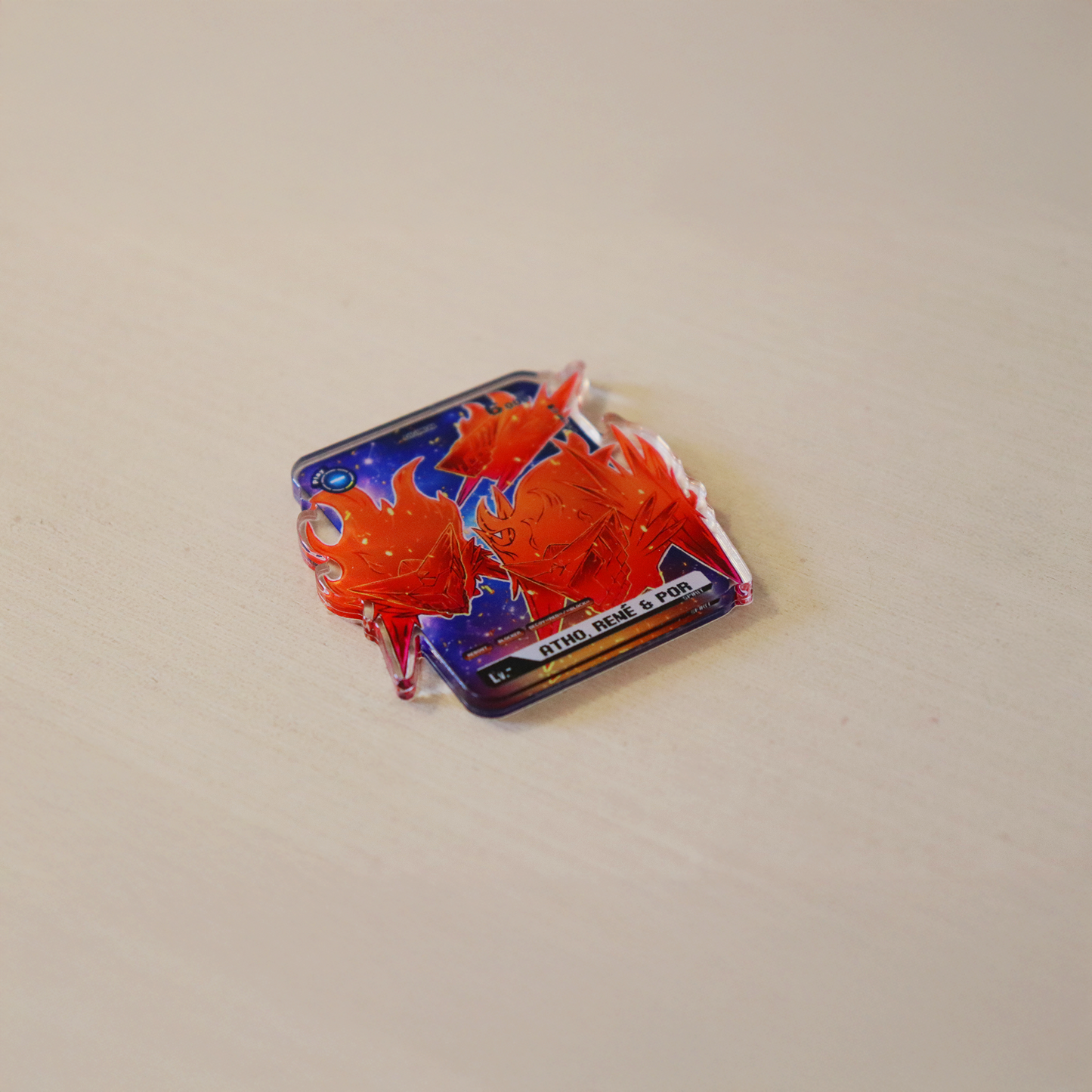 Atho, Rene, and Por acrylic token for a Jesmon Digimon TCG playmat, glossy clear acrylic accessory with red-orange character artwork on a tabletop product photo.